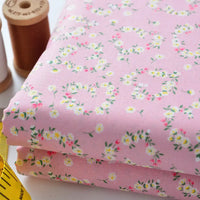 Deux pièces de Longan Craft France Tissu linon de coton fleuri, un voile de coton léger avec des fleurs blanches et jaunes, sont présentées pliées à côté de bobines de fil marron et d'un mètre ruban jaune.