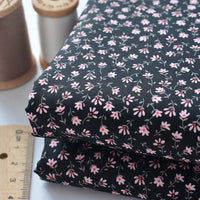 Deux pièces de Tissu linon de coton fleuri au mètre de Longan Craft France, un voile de coton fleuri léger pour les vêtements et les doublures, se trouvent à côté d'une règle en bois et de deux bobines de fil (marron et blanc).