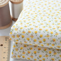 Deux pièces pliées de Tissu linon de coton fleuri au mètre de Longan Craft France, présentant un voile de coton floral jaune, sont présentées à côté d'une règle et de deux bobines de fil (beige et blanc).