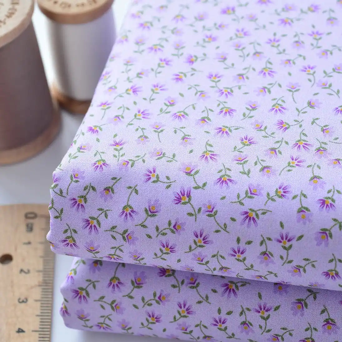 Deux pièces de Tissu linon de coton fleuri au mètre de Longan Craft France, un voile de coton fleuri léger pour les vêtements et les doublures, sont présentées à côté d'une règle en bois et de bobines de fil à coudre.