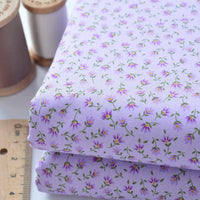 Deux pièces de Tissu linon de coton fleuri au mètre de Longan Craft France, un voile de coton fleuri léger pour les vêtements et les doublures, sont présentées à côté d'une règle en bois et de bobines de fil à coudre.