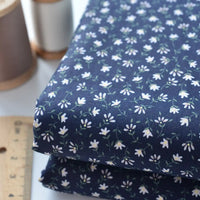 Gros plan sur le Tissu linon de coton fleuri au mètre de Longan Craft France, un voile de coton léger avec un petit motif floral blanc, présenté plié en bleu marine à côté d'une règle en bois et d'une bobine de fil.