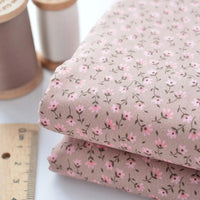 Deux pièces de Tissu linon de coton fleuri de Longan Craft France - un voile de coton marron clair à motif floral rose - sont présentées à côté d'une règle et de deux bobines de fil, parfaites pour les projets de vêtements ou de doublure.
