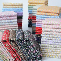 Des piles de tissu linon de coton fleuri de Longan Craft France, un voile de coton léger vendu au mètre pour l'habillement et la doublure, sont soigneusement disposées en rangées dans les couleurs rouge, bleu, vert, jaune, rose et violet avec de petits motifs floraux répétitifs.