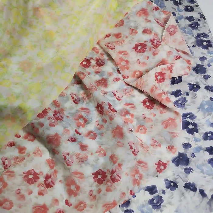 Trois pièces de Longan Craft France Tissu mousseline de soie à imprimé floral au mètre sont disposées : une avec des fleurs jaunes, une avec des fleurs rouges et une avec des fleurs bleues sur fond blanc. Il s'agit d'un tissu léger en soie et coton destiné à la confection de vêtements.