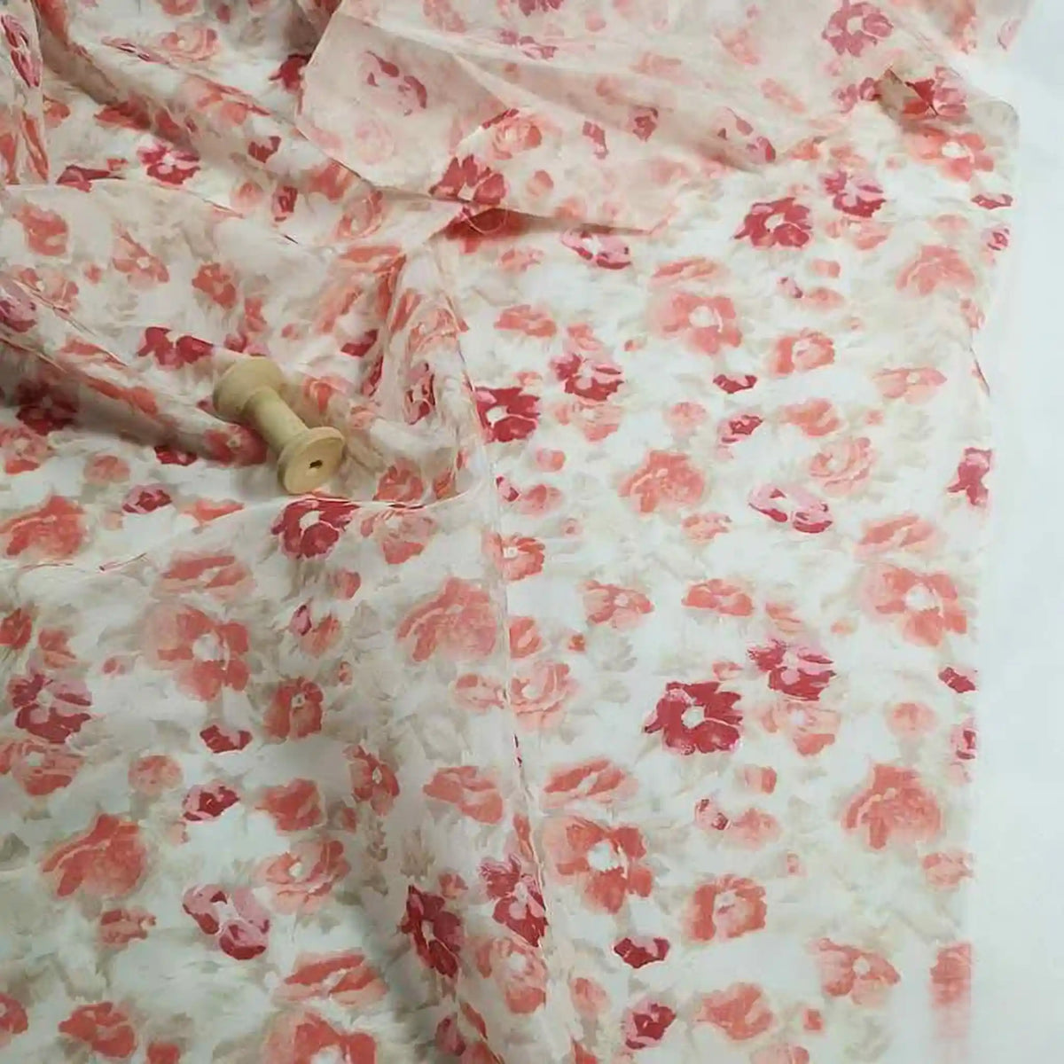 Le Tissu mousseline de soie à imprimé floral de Longan Craft France, une matière légère en soie et coton parfaite pour la confection, est étalé au mètre sur une surface avec deux petites bobines en bois posées dessus.