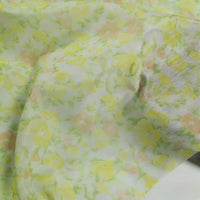 Gros plan sur le tissu mousseline de soie à imprimé floral au mètre de Longan Craft France, un tissu léger en soie et coton avec des fleurs jaunes, vertes et orange clair, aux plis subtils et à la texture délicate.