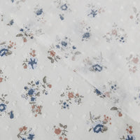 Gros plan sur le tissu plumetis à imprimé floral au mètre en blanc de Longan Craft, qui présente un plumetis de coton léger avec une texture légèrement transparente et des motifs floraux bleus, rouges et bruns dispersés.