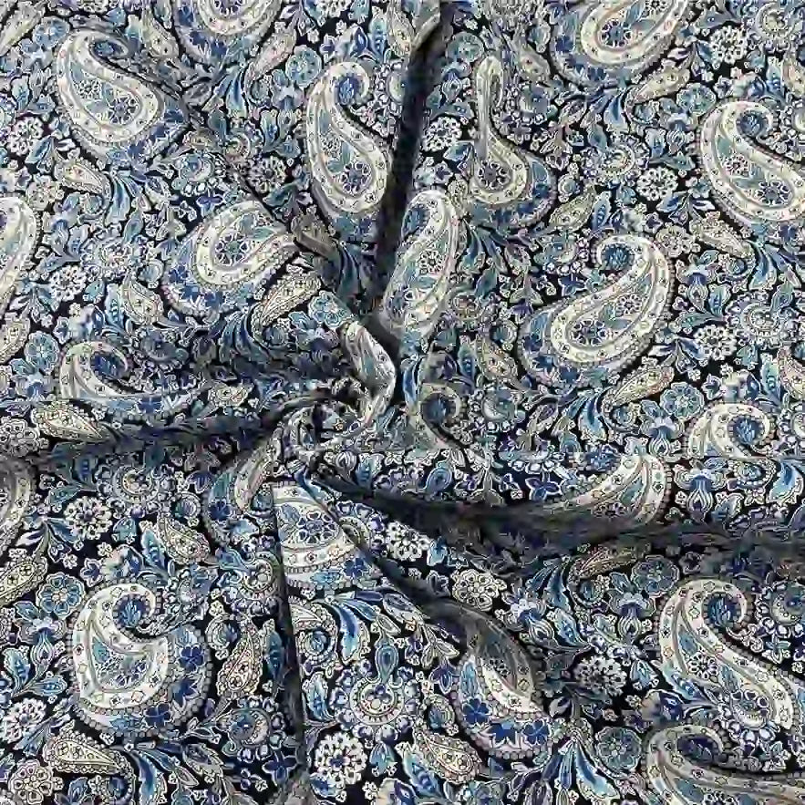 Gros plan sur le Tissu motif paisley en coton imprimé floral au mètre de Longan Craft France, présenté en bleu et blanc avec des plis froncés. Ce tissu léger et agréable au toucher est parfait pour créer des accessoires élégants.