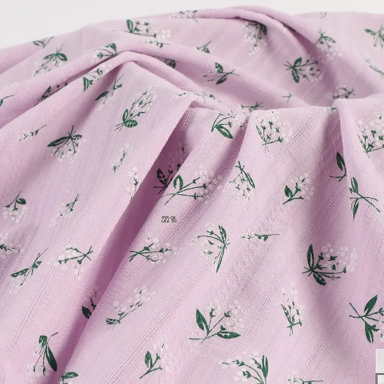 Découvrez notre tissu dobby coton doux Longan Craft France, imprimé au mètre avec un motif floral vert et blanc sur fond rose clair, idéal pour vêtements.