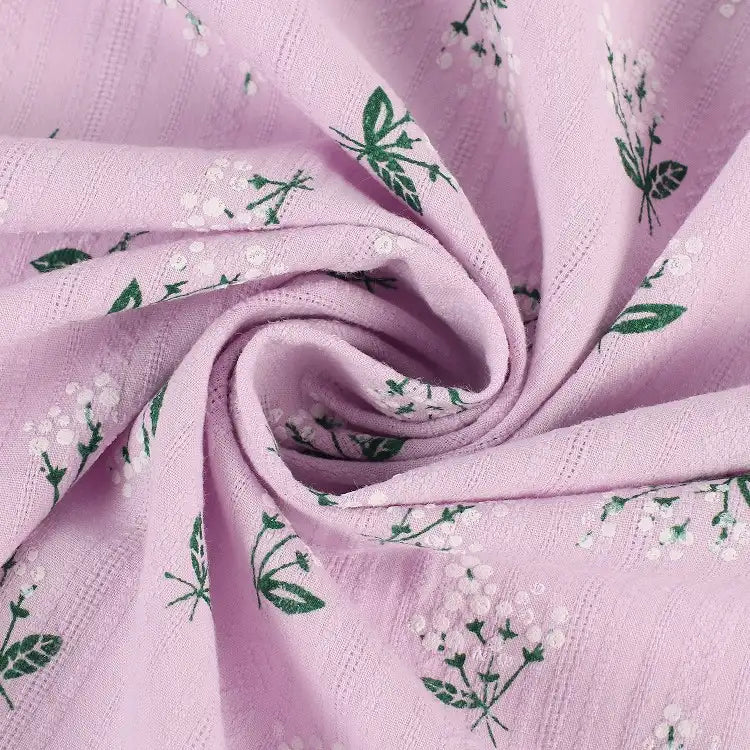 Gros plan sur le tissu dobby imprimé floral au mètre de Longan Craft France en violet clair, avec des rayures subtiles et un motif de petites fleurs blanches et de feuilles vertes, torsadées en spirale. Parfait pour les vêtements en coton doux.