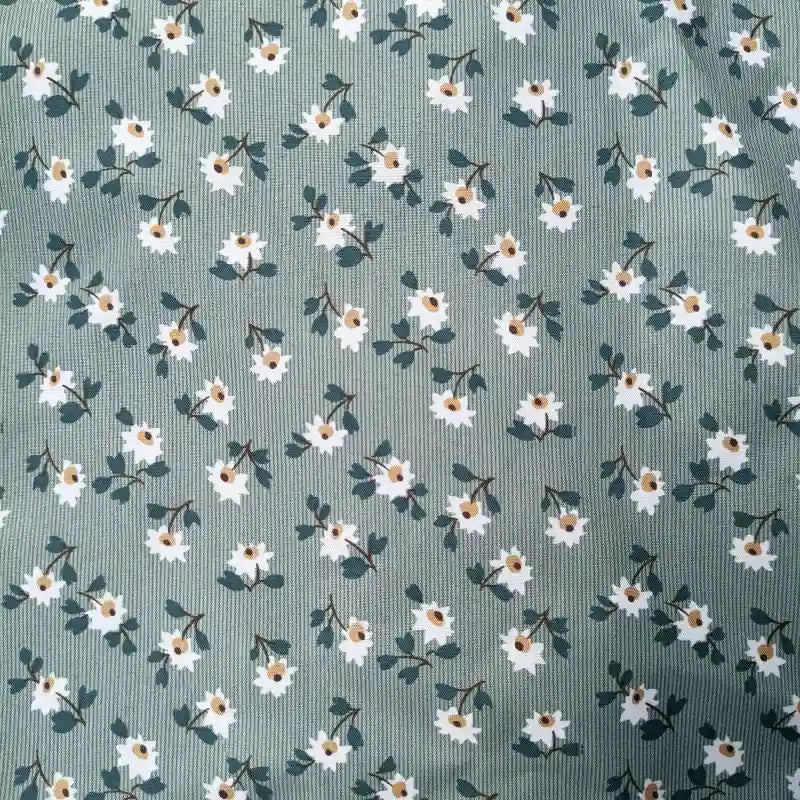 Un gros plan de Tissu peau de pêche imprimé floral de Longan Craft France montre de petites fleurs blanches et des feuilles vertes foncées sur un fond vert mat - un polyester microfibre doux, régulièrement espacé, parfait pour coudre des vêtements confortables.