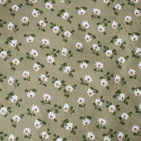 Le Tissu peau de pêche imprimé floral au mètre de Longan Craft France est un polyester microfibre avec des petites fleurs blanches au centre jaune et des feuilles vertes sur un vert olive clair. Sa texture douce est idéale pour des projets de couture élégants.
