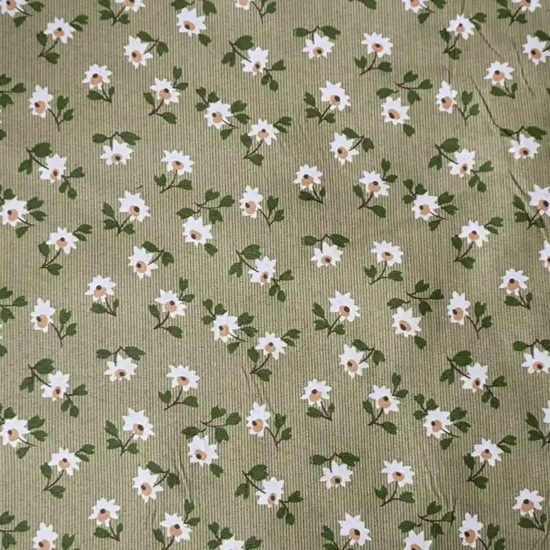 Le Tissu peau de pêche imprimé floral au mètre de Longan Craft France est un polyester microfibre avec des petites fleurs blanches au centre jaune et des feuilles vertes sur un vert olive clair. Sa texture douce est idéale pour des projets de couture élégants.