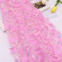Gros plan sur le Tissu sequin floral au mètre de Longan Craft France, un brodé scintillant résille à sequins en relief pour accessoires de robe, présenté sur des papiers blancs à côté de tulipes jaunes.