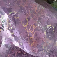 Gros plan sur le Tissu sequin floral au mètre de Longan Craft France : résille lavande transparente avec des fleurs en paillettes en relief et des broderies irisées, parfaite pour les robes décoratives ou les accessoires.
