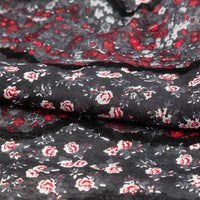 Un gros plan du tissu en jersey coton imprimé fleurs et animaux au mètre de Longan Craft France montre de petites fleurs rouges et blanches avec des accents gris sur un tissu noir 100 % coton, légèrement froissé et texturé - idéal pour les robes et les vêtements.