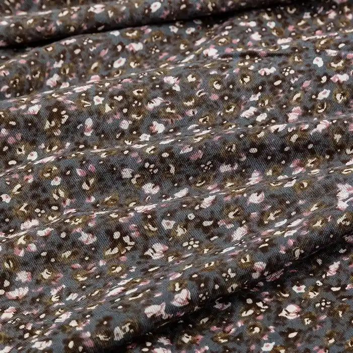 Gros plan sur le tissu en jersey coton imprimé fleurs et animaux de Longan Craft France, montrant de petits motifs floraux et animaux en blanc, rose et marron clair sur un jersey de coton doux à la texture visible et aux plis délicats.