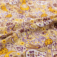 Un gros plan sur le Tissu jersey imprimé paisley au mètre de Longan Craft France révèle des motifs détaillés jaunes, bruns et violets avec de petites fleurs sur un jersey 100 % coton légèrement plié - parfait pour des peignoirs ou des chemisiers élégants.