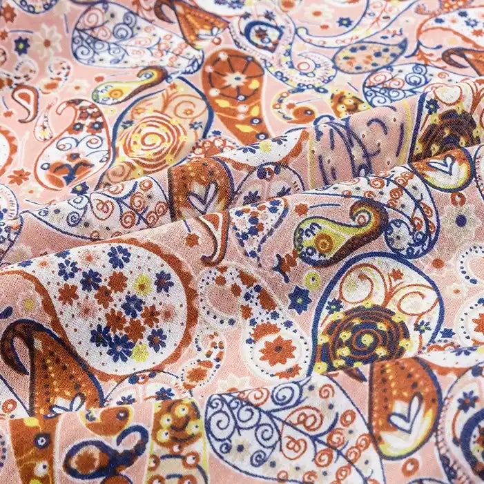 Gros plan sur le Tissu jersey imprimé paisley au mètre de Longan Craft France, qui présente des motifs bruns, bleus et jaunes sur un jersey 100 % coton rose pâle - idéal pour les chemisiers et mettant en valeur la texture de ce tissu élégant.