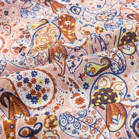 Gros plan sur le Tissu jersey imprimé paisley au mètre de Longan Craft France, qui présente des motifs bruns, bleus et jaunes sur un jersey 100 % coton rose pâle - idéal pour les chemisiers et mettant en valeur la texture de ce tissu élégant.