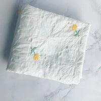 Un morceau plié du tissu coton brodé ajouré à fleurs au mètre de Longan Craft France, un tissu de coton blanc avec une délicate broderie florale, repose sur une surface en marbre clair.