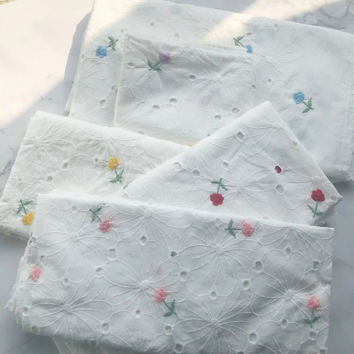 Trois pièces pliées de Tissu coton brodé ajouré à fleurs de Longan Craft France, un tissu de coton blanc doux avec des broderies florales, sont disposées sur une surface légère - idéale pour les robes et disponible au mètre.