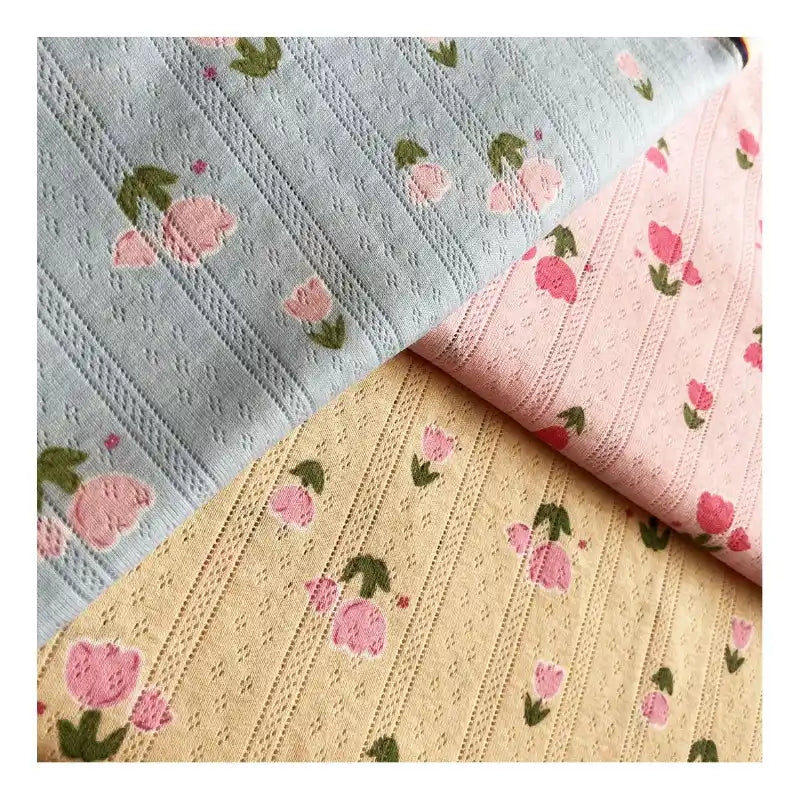 La maille pointelle imprimée tulipes au mètre de Longan Craft France : trois tissus jacquard doux (bleu clair, rose, jaune pâle), chacun avec un petit œillet et des rangées de tulipes roses avec des feuilles vertes - idéal pour les tops, les shorts ou les pyjamas DIY d'été.