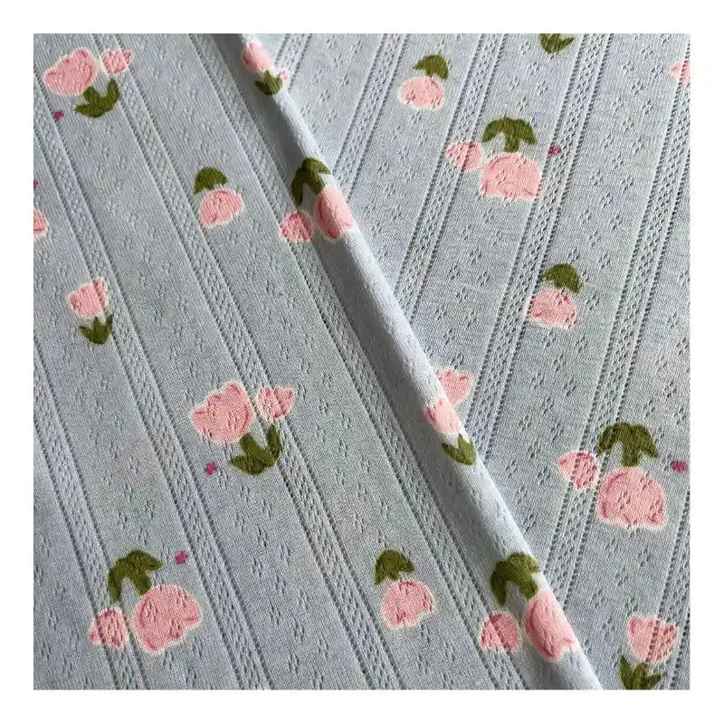 Tissu pointelle jacquard bleu clair de Longan Craft France, présentant des rayures gaufrées, des motifs à points et de petits motifs de tulipes roses avec des feuilles vertes. Vendu au mètre - idéal pour coudre des hauts, des shorts ou des pyjamas. Couture diagonale visible.