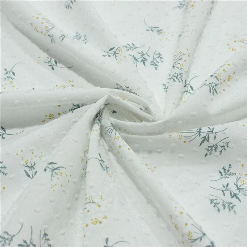 Tissu plumetis fleuri au mètre de Longan Craft France : tissu blanc avec texture à pois, imprimé de petites feuilles vertes et motifs fleuris jaunes, disponible en spirale.