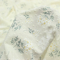 Gros plan sur le Tissu plumetis fleuri au mètre de Longan Craft France : un coton crème léger avec un motif texturé en pointillés et de délicates fleurs blanches et jaunes - doux, léger et idéal pour les robes d'été.