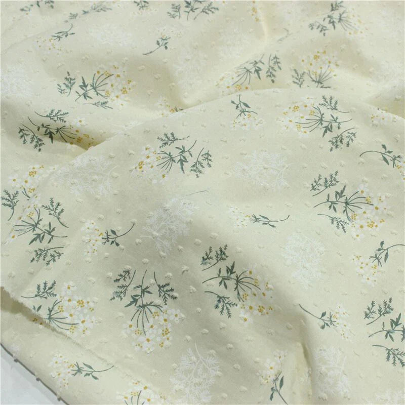 Découvrez le tissu plumetis fleuri au mètre Longan Craft France : un coton imprimé blanc et jaune, à texture légère et pois discrets, orné de petites fleurs blanches et jaunes avec tiges vertes. Parfait pour une robe d'été.