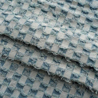 Gros plan sur le tissu denim à franges au mètre de Longan Craft France : un tissu en jean effiloché bleu et gris avec un motif en damier texturé, des bords effilochés et un design en couches - idéal pour les projets de couture décoratifs.