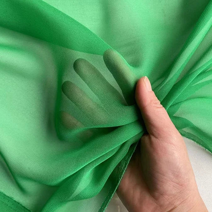 Une main présente la Georgette de soie au mètre de Longan Craft France, en déroulant ce crêpe de soie 100% mûrier (8 mommes), léger et diaphane, dont le tissu souple et translucide laisse apparaître les doigts grâce à un drapé fluide.