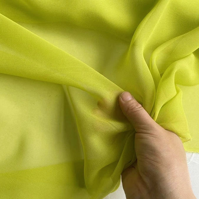 Une main fronce la Georgette de soie au mètre vert lime de Longan Craft France - un crêpe de soie 100 % mûrier de 8 mamans, réputé pour sa transparence et son drapé doux et fluide.