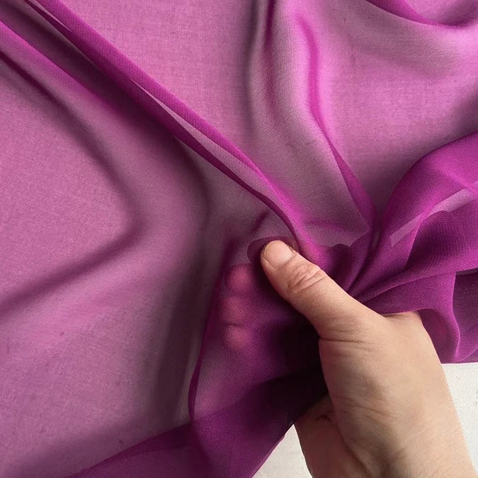 Une main tient la Georgette de soie au mètre de Longan Craft France - 100 % soie de mûrier, 8 mètres - qui met en valeur son drapé fluide et sa texture translucide et légère sur un fond uni.