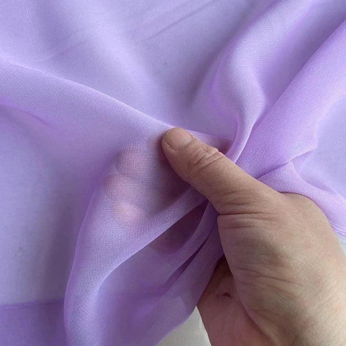 Une main tient et rassemble la Georgette de soie au mètre de Longan Craft France, un crêpe diaphane 100 % soie de mûrier (8 mommes), mettant en valeur sa texture translucide, douce et fluide, idéale pour le drapé.