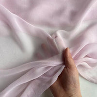 Une main présente le Georgette de soie au mètre-8 mommes de Longan Craft France, 100 % soie de mûrier sur blanc, soulignant le drapé aérien et la texture diaphane et délicate de ce tissu de crêpe de soie de qualité supérieure.