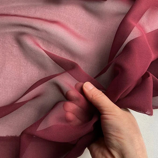 Une main tient et froisse délicatement la Georgette de soie au mètre de Longan Craft France, 100% soie de mûrier (8 mommes), laissant la lumière révéler sa texture douce, fluide et translucide, idéale pour les drapés.