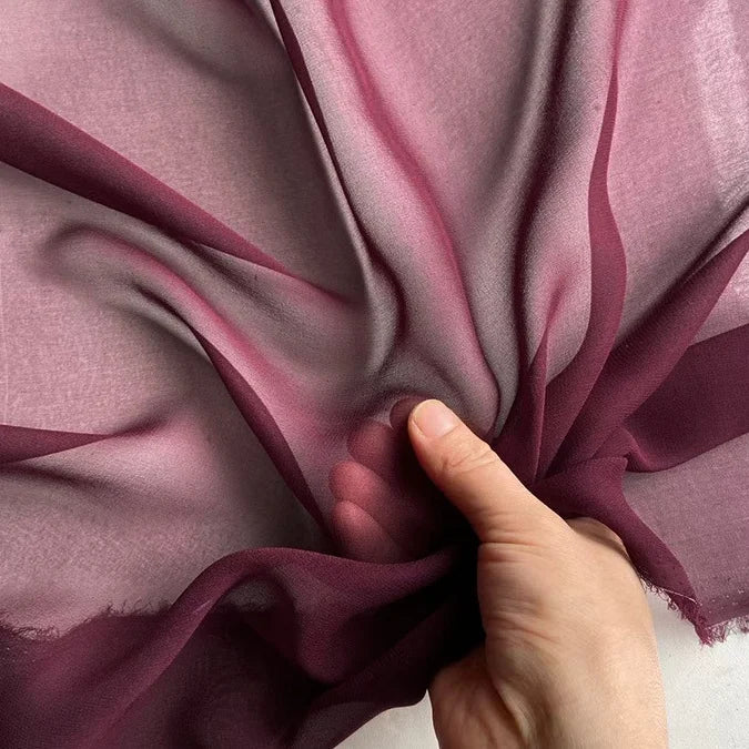 Une main met en valeur la texture légère et translucide de la Georgette de soie au mètre de Longan Craft France - un crêpe de 8 mm, 100 % soie de mûrier, idéal pour un drapé fluide - sur un fond clair.