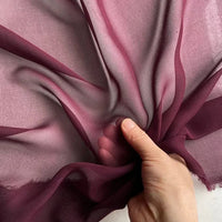 Une main met en valeur la texture légère et translucide de la Georgette de soie au mètre de Longan Craft France - un crêpe de 8 mm, 100 % soie de mûrier, idéal pour un drapé fluide - sur un fond clair.