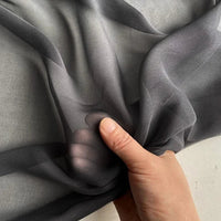 Une main fronce la Georgette de soie au mètre de Longan Craft France : 100% crêpe de soie de mûrier (8 mommes), souple et fluide pour le drapé. Son tissu noir est légèrement transparent, révélant le contour des doigts à travers sa texture délicate.