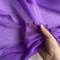 Une main rassemble un morceau de Georgette de soie au mètre de Longan Craft France, fabriquée à partir de 100 % de soie de mûrier (8 mommes). Ce tissu léger, transparent et fluide révèle les doigts grâce à son drapé délicat.