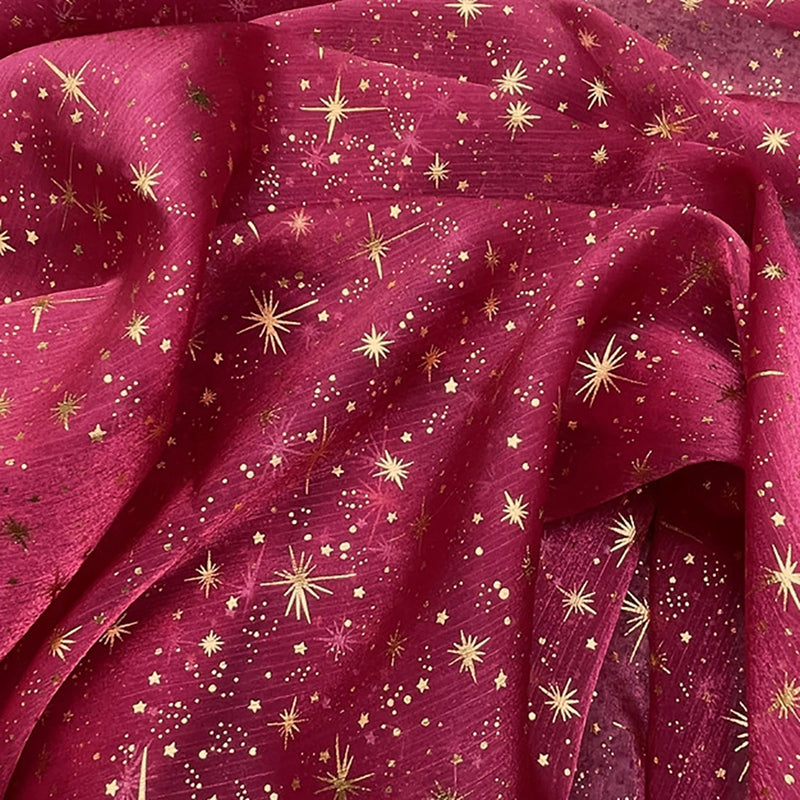 Découvrez le tissu organza étoilé au mètre de Longan Craft France : un organza imprimé bordeaux décoré d'étoiles et de points dorés, légèrement transparent et souple, idéal pour robes de mariée et costumes de mariage.