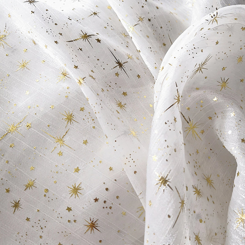 Le Tissu organza étoilé au mètre de Longan Craft France est un organza blanc imprimé de motifs étoiles dorées, souple et brillant, parfait pour la confection de robes de mariée et costumes de mariage.