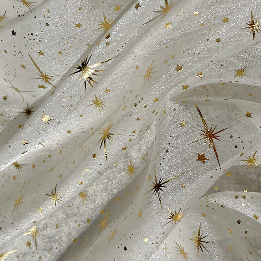 Gros plan sur le Tissu organza étoilé au mètre de Longan Craft France, un tissu blanc transparent orné d'étoiles et d'éclats dorés. Sa texture légèrement froissée crée des plis doux et un effet chatoyant, idéal pour les robes de mariée et les costumes de mariage.