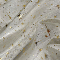 Gros plan sur le Tissu organza étoilé au mètre de Longan Craft France, un tissu blanc transparent orné d'étoiles et d'éclats dorés. Sa texture légèrement froissée crée des plis doux et un effet chatoyant, idéal pour les robes de mariée et les costumes de mariage.