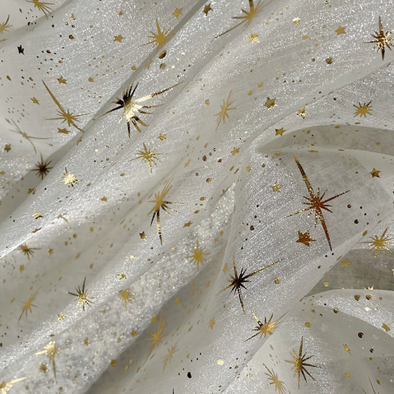 Gros plan sur le Tissu organza étoilé au mètre de Longan Craft France, un tissu blanc transparent orné d'étoiles et d'éclats dorés. Sa texture légèrement froissée crée des plis doux et un effet chatoyant, idéal pour les robes de mariée et les costumes de mariage.