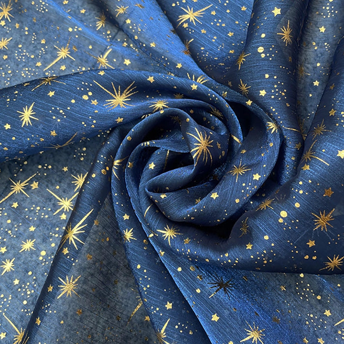 Le Tissu organza étoilé au mètre de Longan Craft France est un tissu organza imprimé bleu orné d'étoiles et de points dorés, idéal pour la confection de robes de mariée et de costumes.