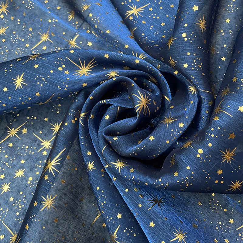 Le Tissu organza étoilé au mètre de Longan Craft France est un tissu organza imprimé bleu orné d'étoiles et de points dorés, idéal pour la confection de robes de mariée et de costumes.